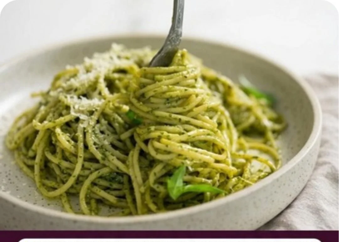 A bowl of glossy pesto pasta with fresh basil and pine nuts