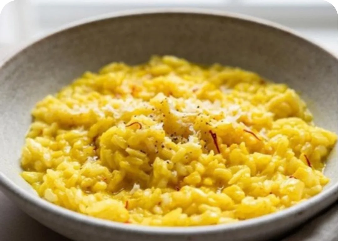 A bowl of saffron risotto with a silky golden finish garnished with herbs.